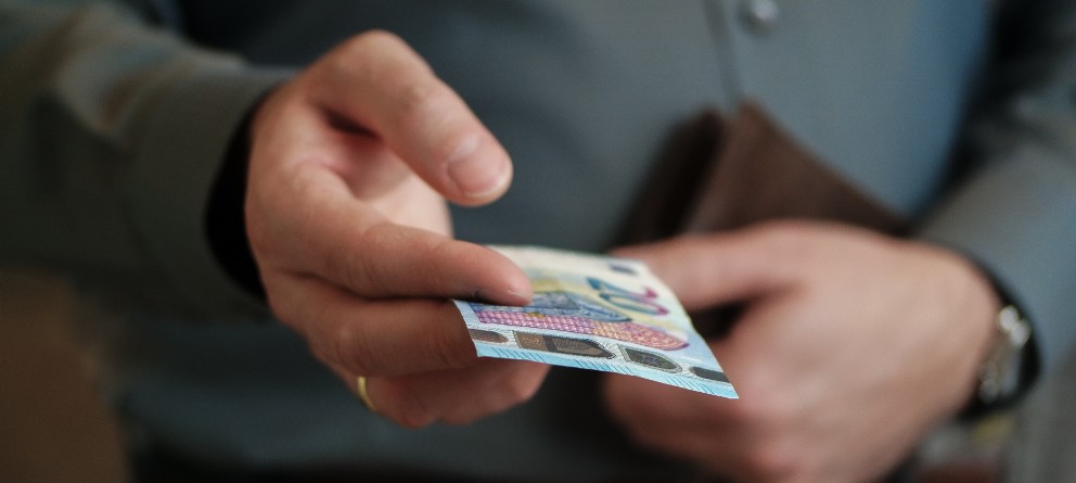 Mano de caballero sujetando ofreciendo un billete de 20 euros. Llevar algo de dinero en efectivo es uno de los tips de como preparar tu viaje largo. | eligetucoche.es